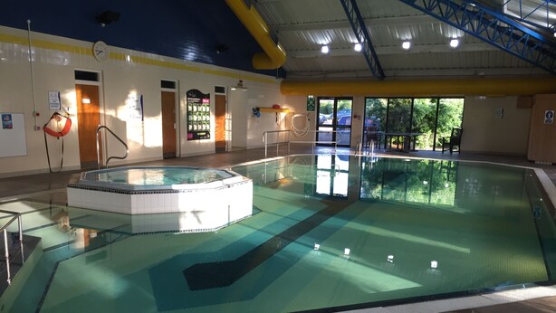 An indoor swimming pool with a hot tub, clear water, and tiled flooring.