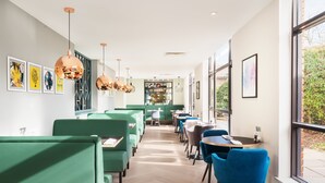 A modern restaurant with green booths and blue chairs, large windows, and artwork on the walls.