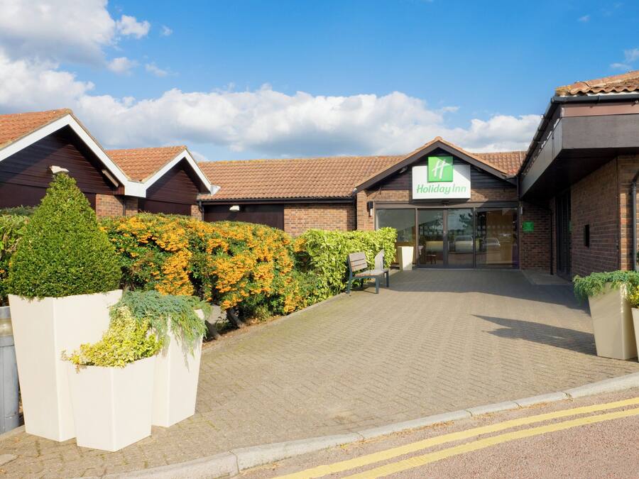 A Holiday Inn hotel entrance with a brick facade, a tiled roof, and a paved driveway leading to the entrance.
