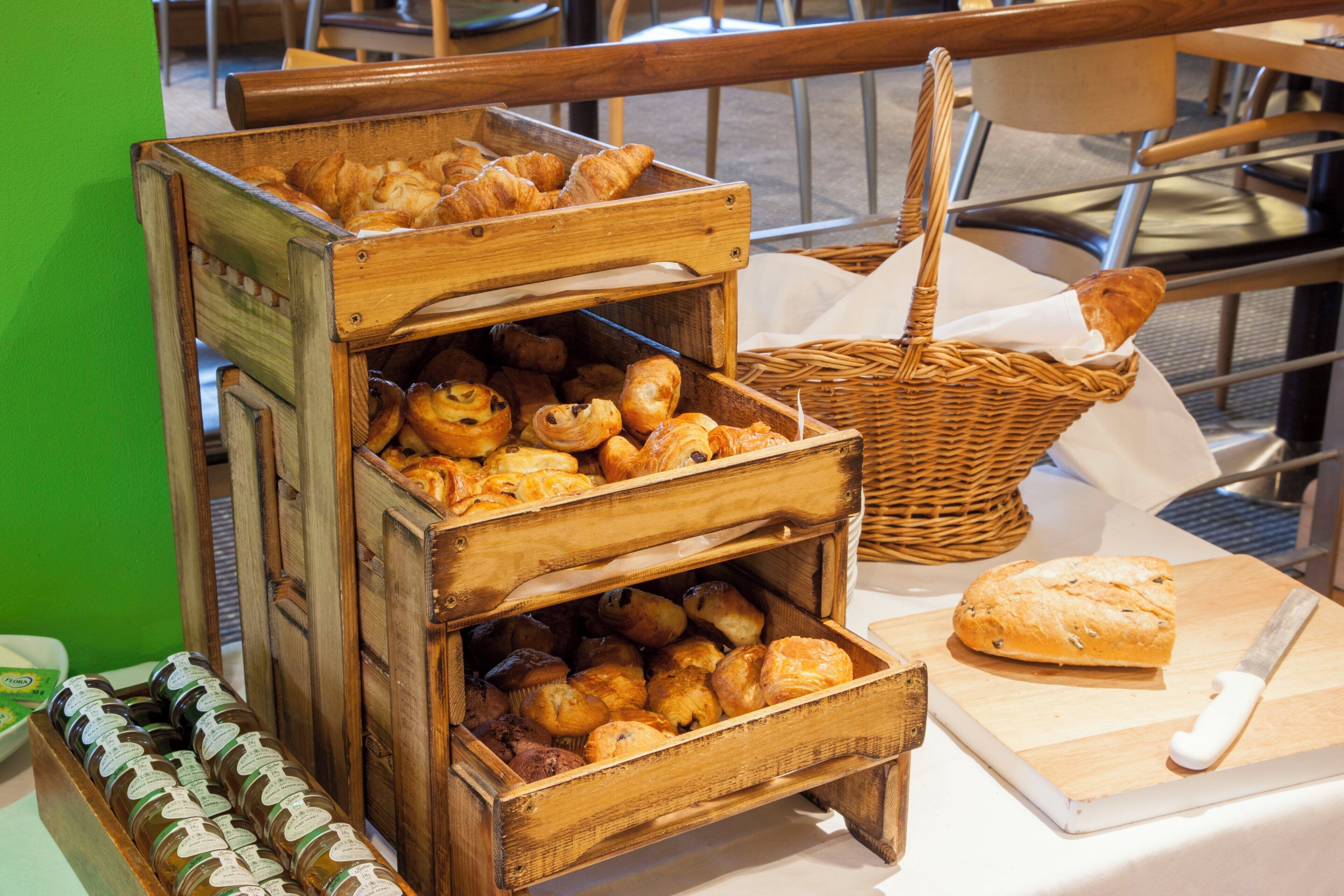 A wooden display case with various baked goods, a wicker basket, and a loaf of bread on a cutting board.