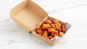 An open cardboard box containing glazed chicken nuggets on a marble surface.