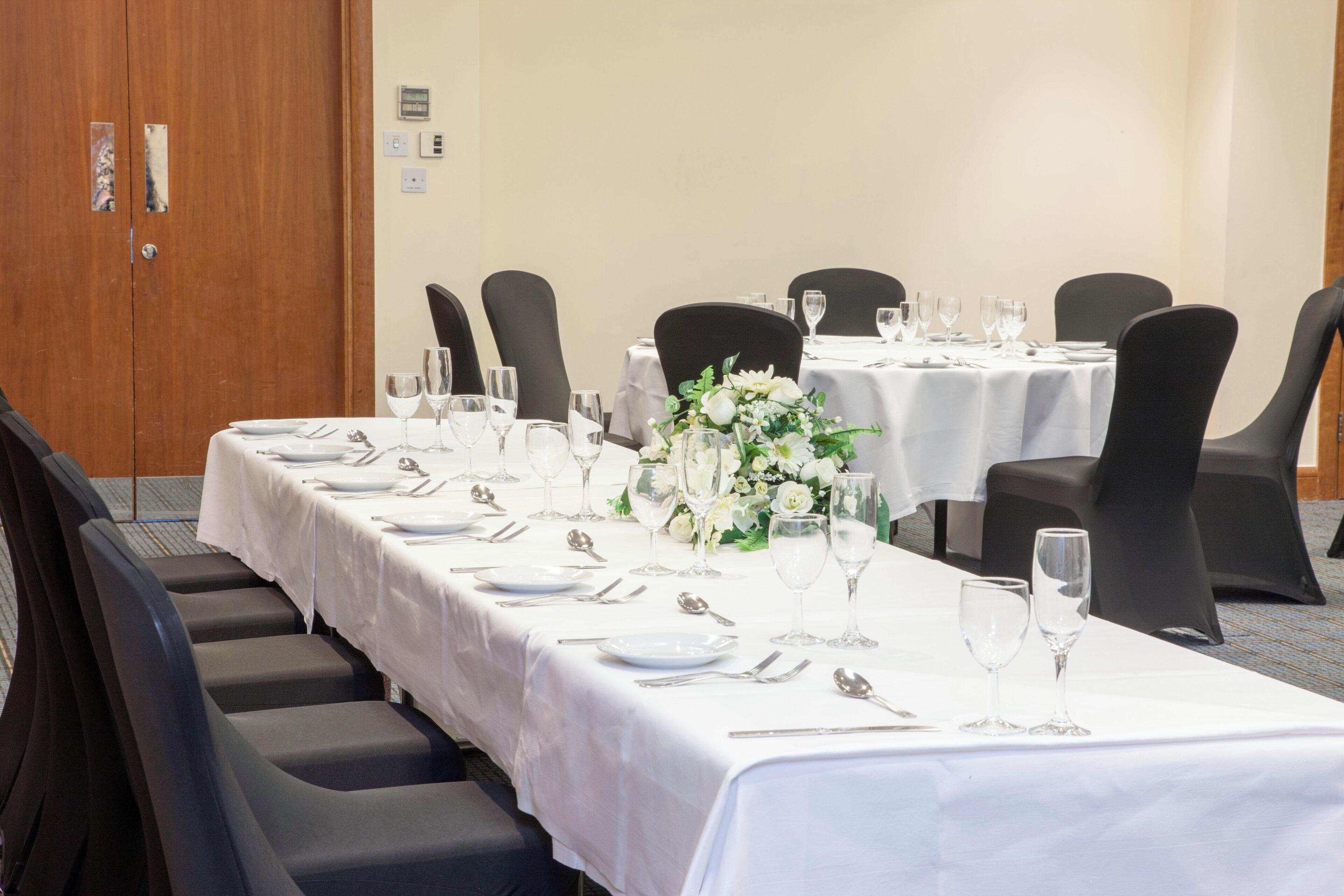 Un salón de conferencias con mesas dispuestas para un evento formal, equipado con sillas, mesas y copas.