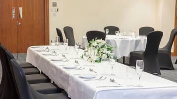 Un salón de conferencias con mesas dispuestas para un evento formal, equipado con sillas, mesas y copas.