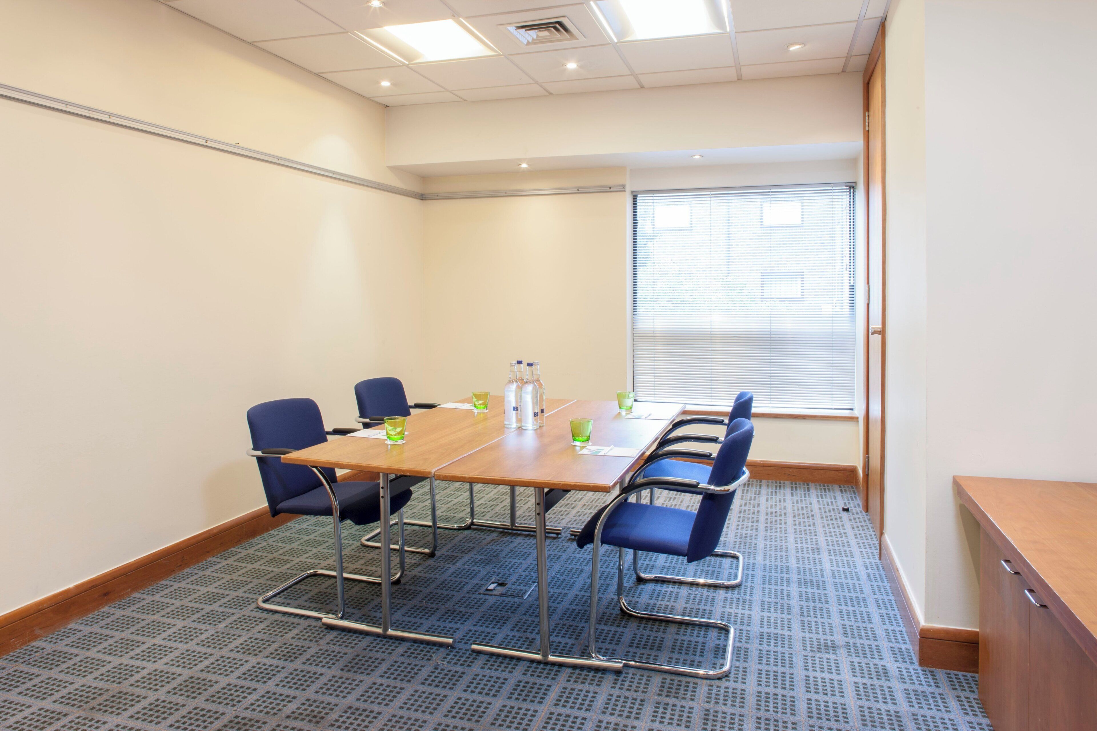 A conference room with a long table, six chairs, and a window with blinds.