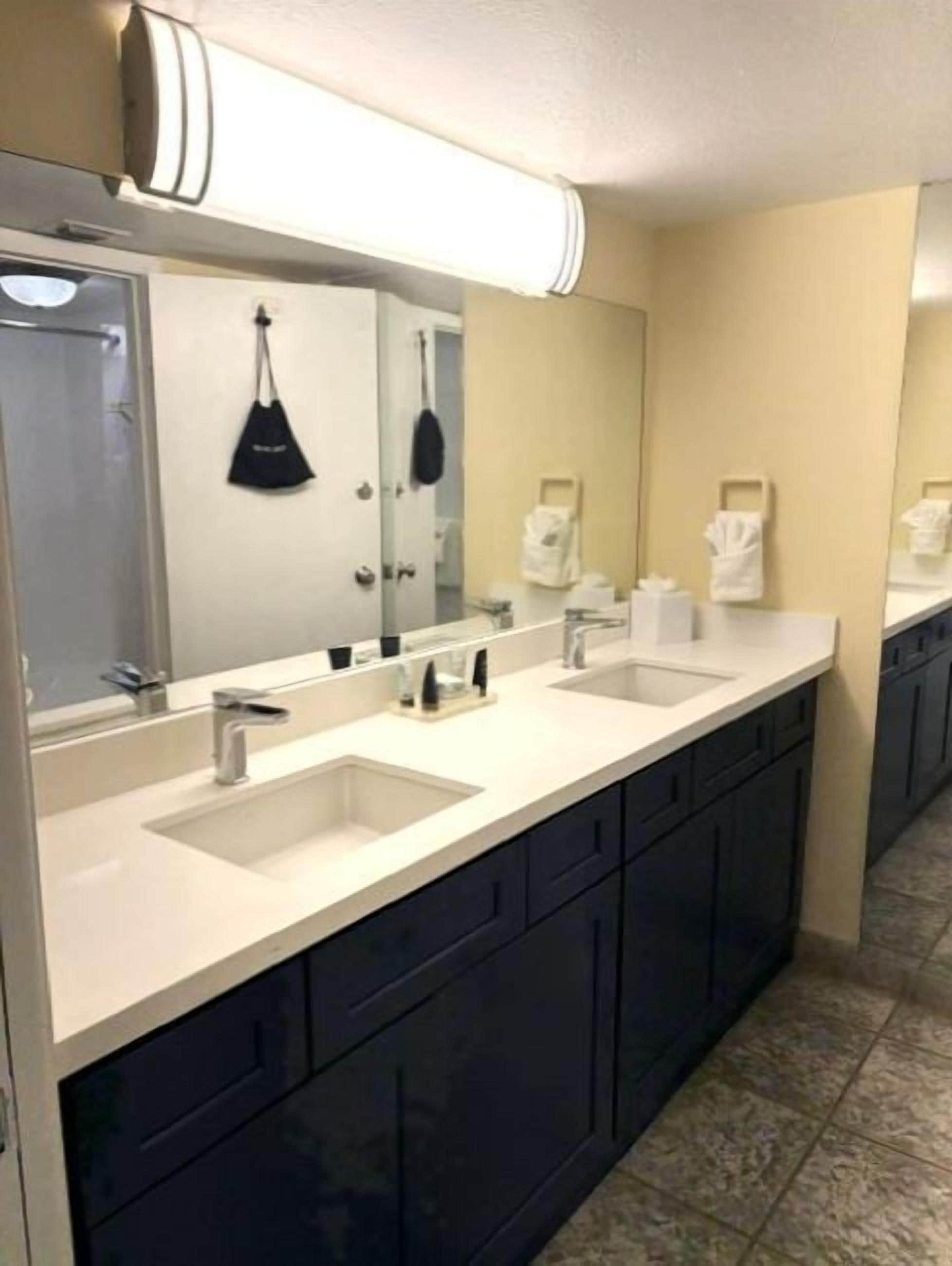 A hotel bathroom with a long counter, two sinks, a large mirror, and a towel rack.