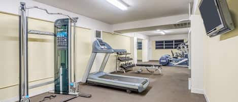 Un gimnasio con cinta de correr, banco de pesas y diversas máquinas de ejercicio.