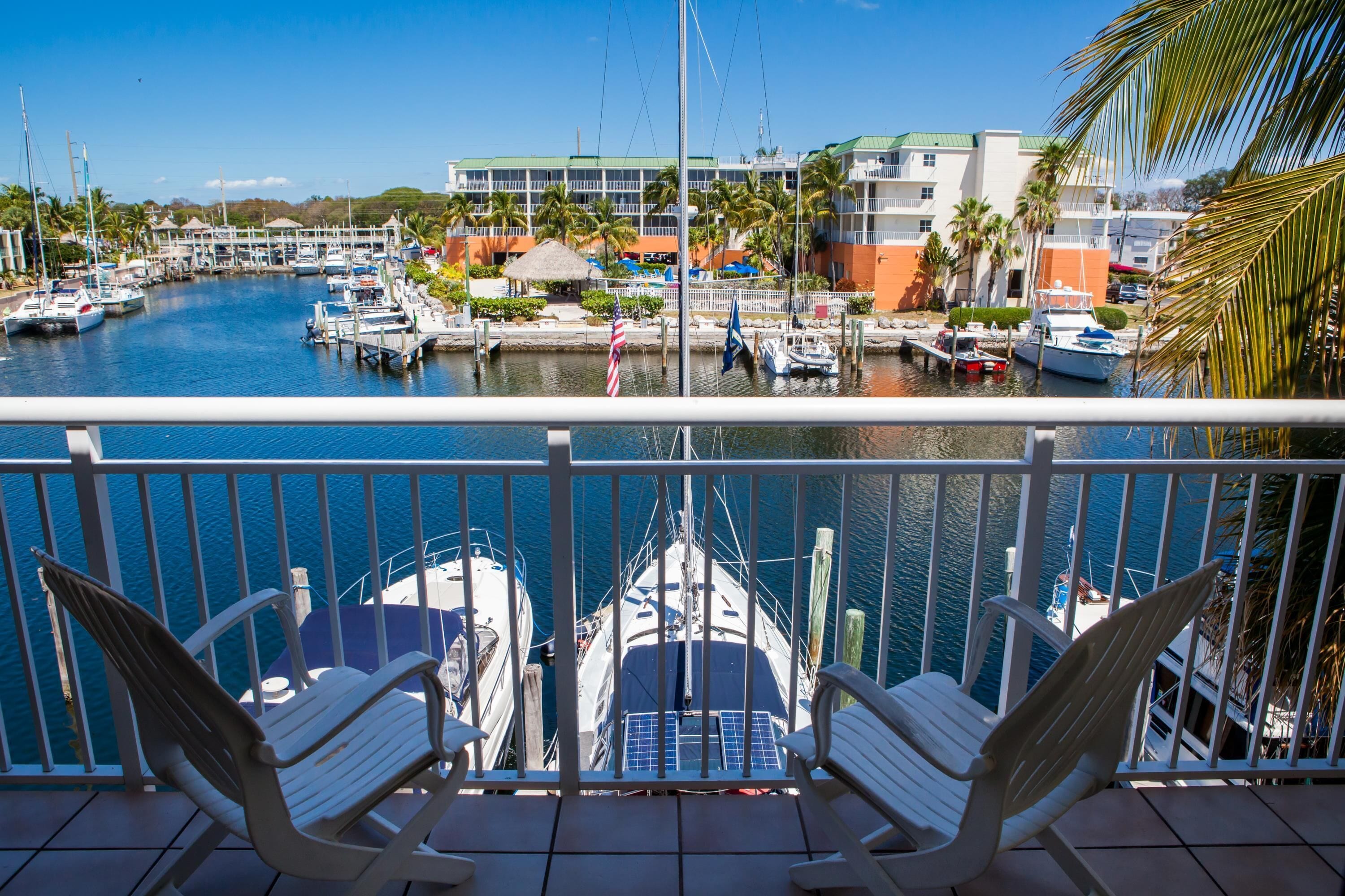 A marina with boats docked, a building with a green roof, and a palm tree.