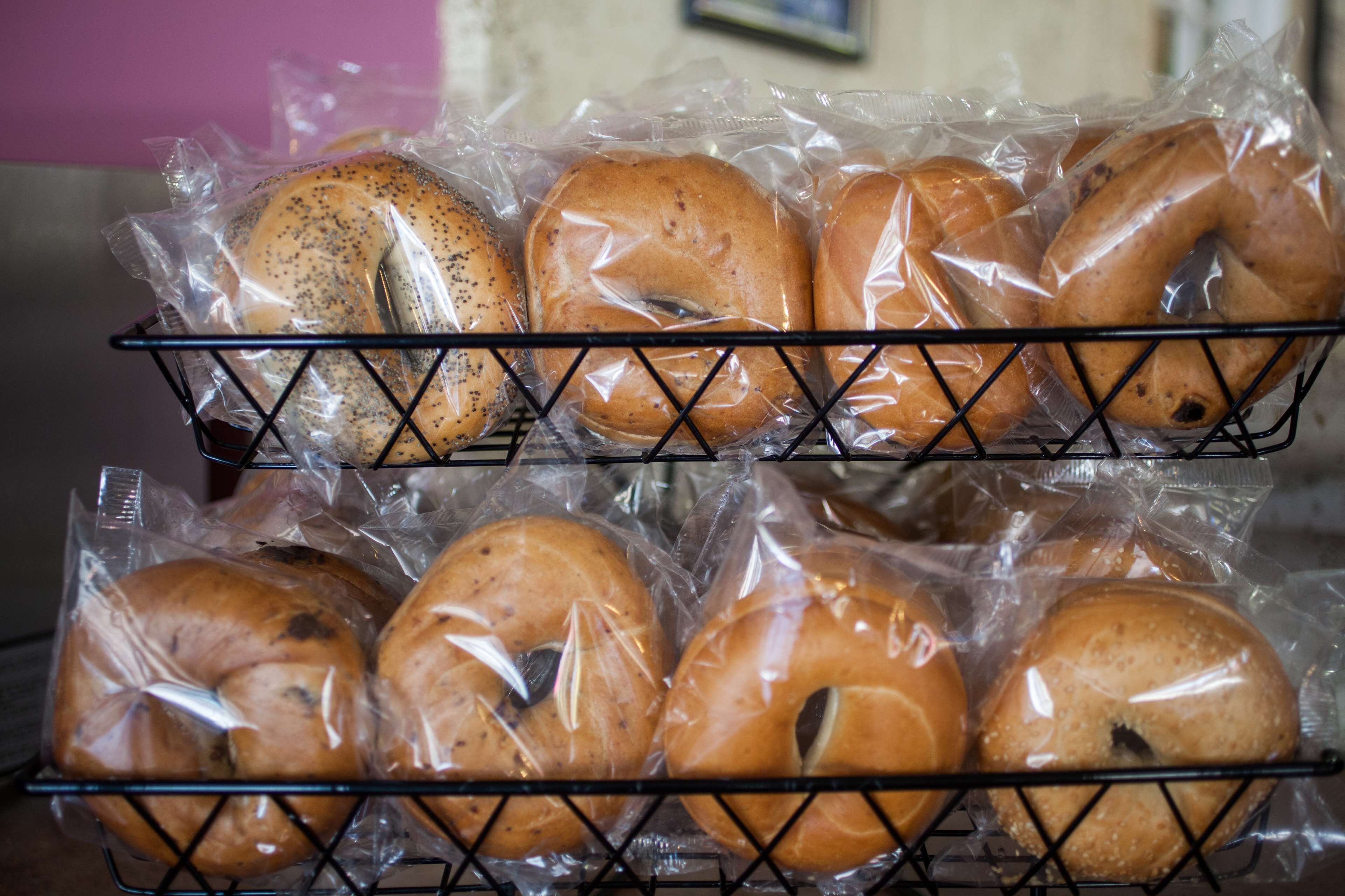 A wire basket containing several plastic-wrapped bagels.