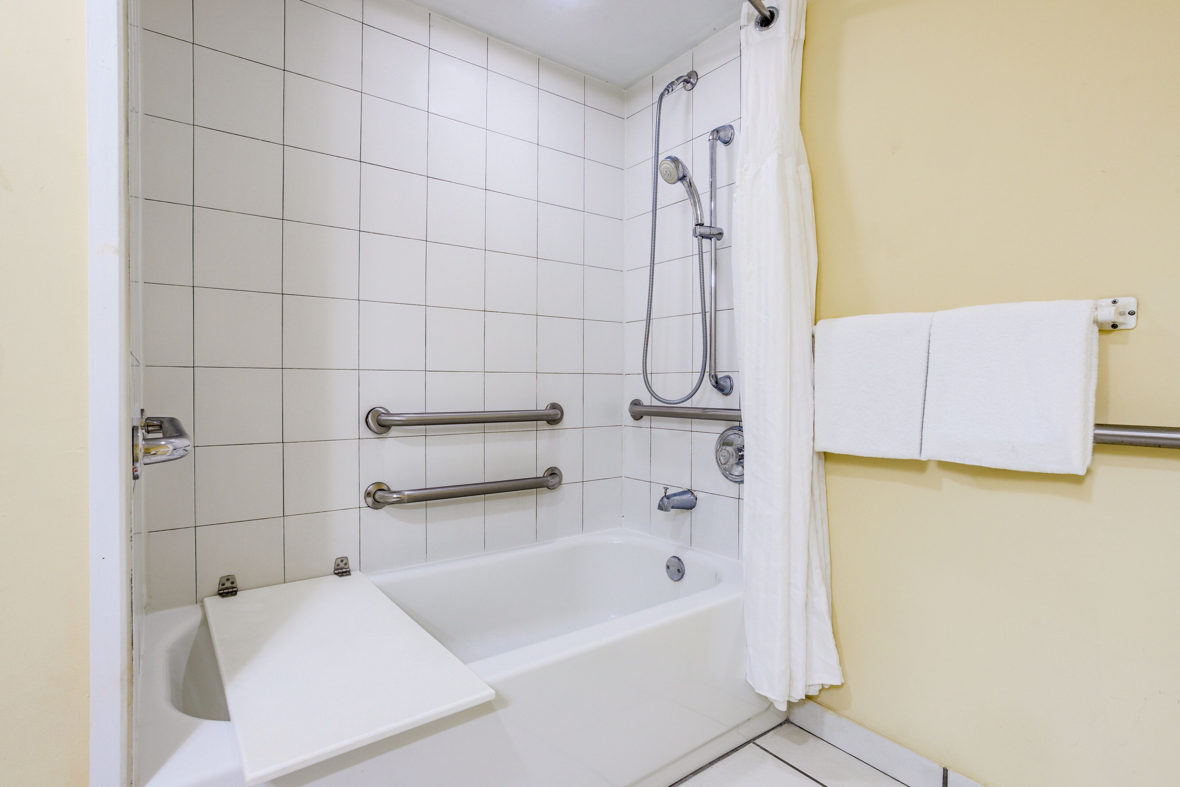 A standard bathroom with a bathtub, shower, and handrails.