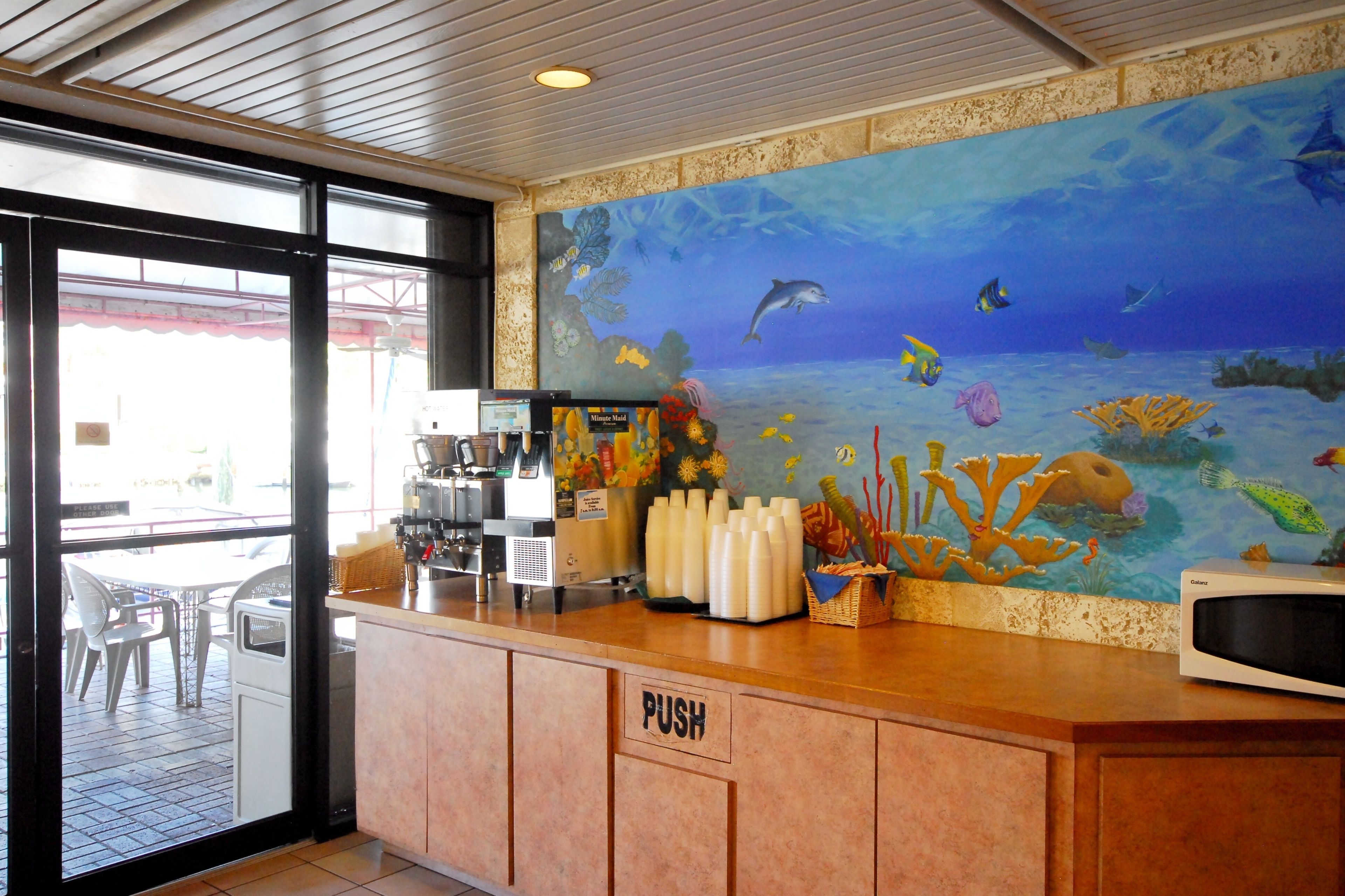 Balcão de restaurante com uma placa de 'PUSH', uma máquina de café e um mural com tema de fundo marinho.