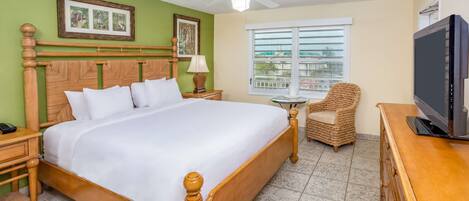 A hotel room with a wooden bed, a television, a wicker chair, and a window with a view.