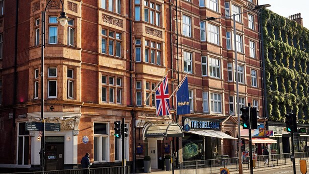 A historic red brick building with multiple stories, featuring a prominent corner entrance and a flag. - Thistle London Bloomsbury Park (London)