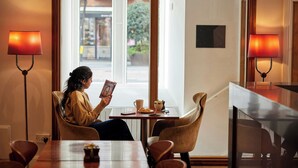 A person reading a magazine at a table with a window view, two lamps, and a bowl of fruit. - Thistle London Bloomsbury Park (London)