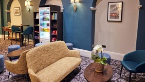 A lobby with a sofa, chairs, a bar area, and a refrigerator stocked with beverages. - Thistle London Bloomsbury Park (London)