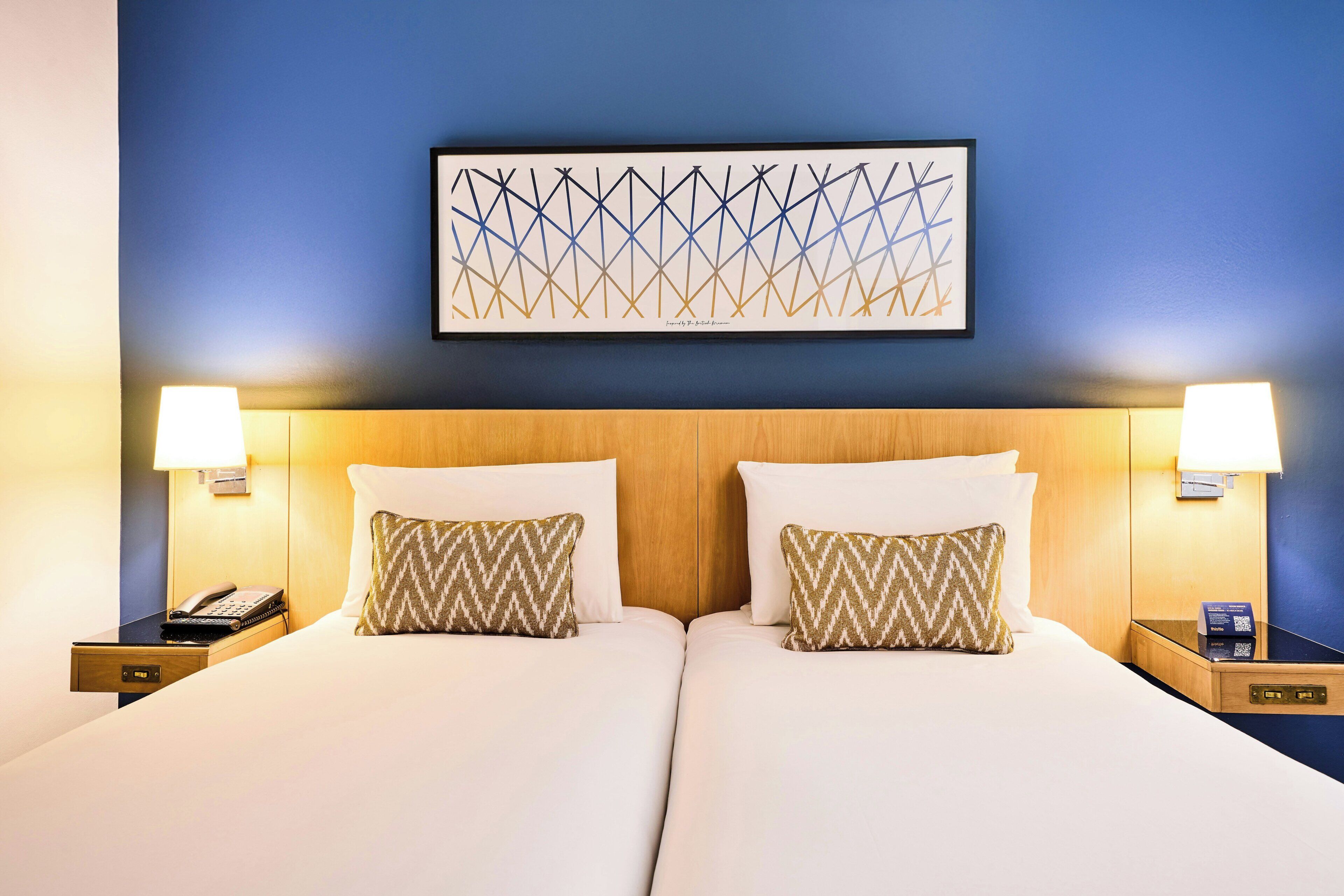 A double bed with two pillows, a headboard, bedside tables with lamps, and a framed abstract artwork on the wall.