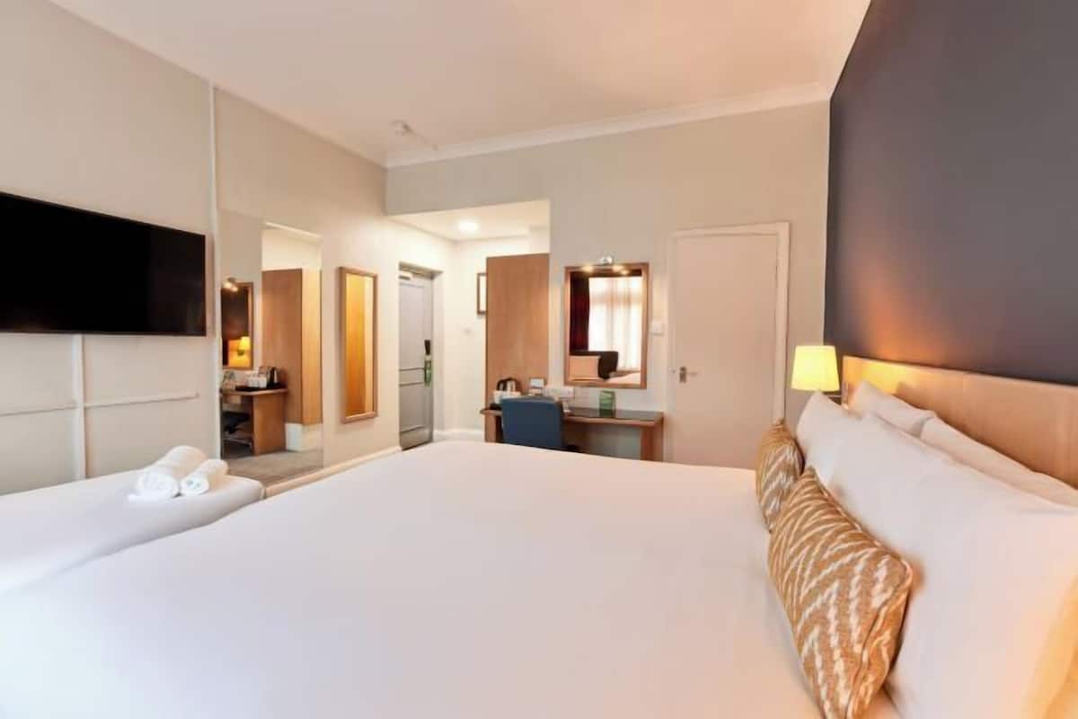 Habitación de hotel con una cama grande, un escritorio, una silla, un televisor montado en la pared y un espejo.