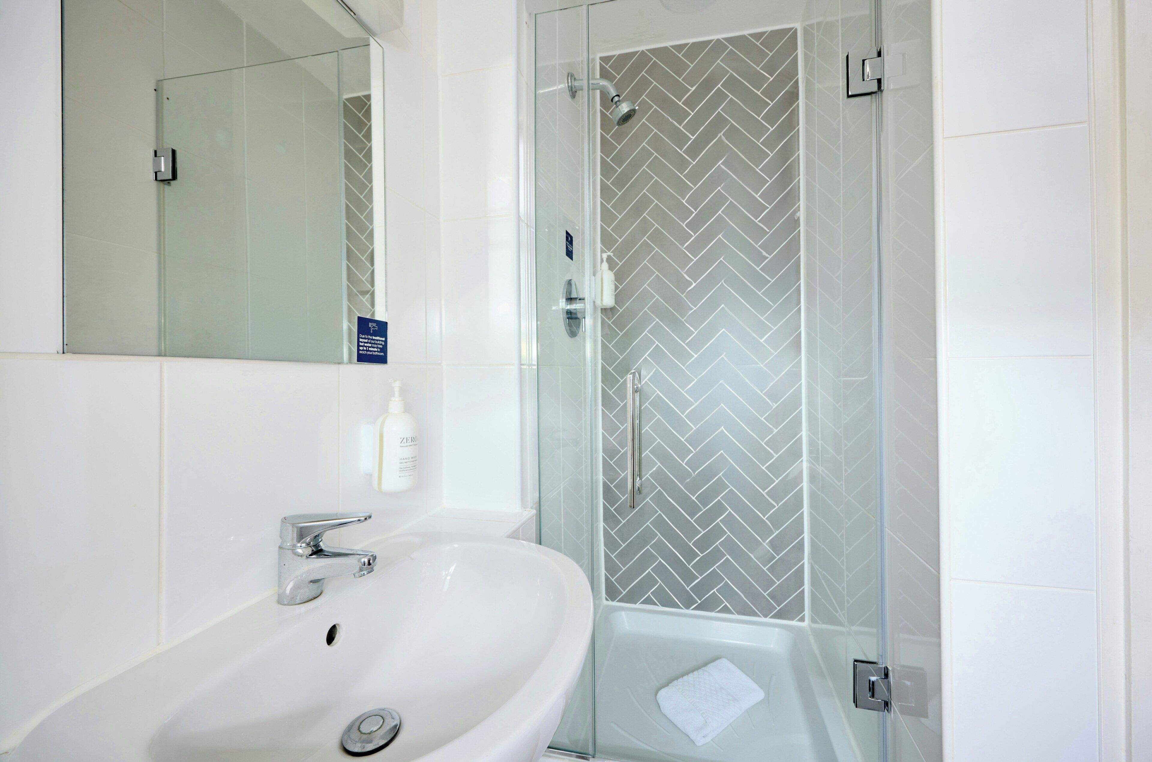 A modern bathroom with a white sink, a glass-enclosed shower, and a herringbone-patterned tile wall.