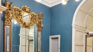 A room with a blue wall, a gold ornate mirror, a yellow sofa, and a round table. - Thistle London Bloomsbury Park (London)