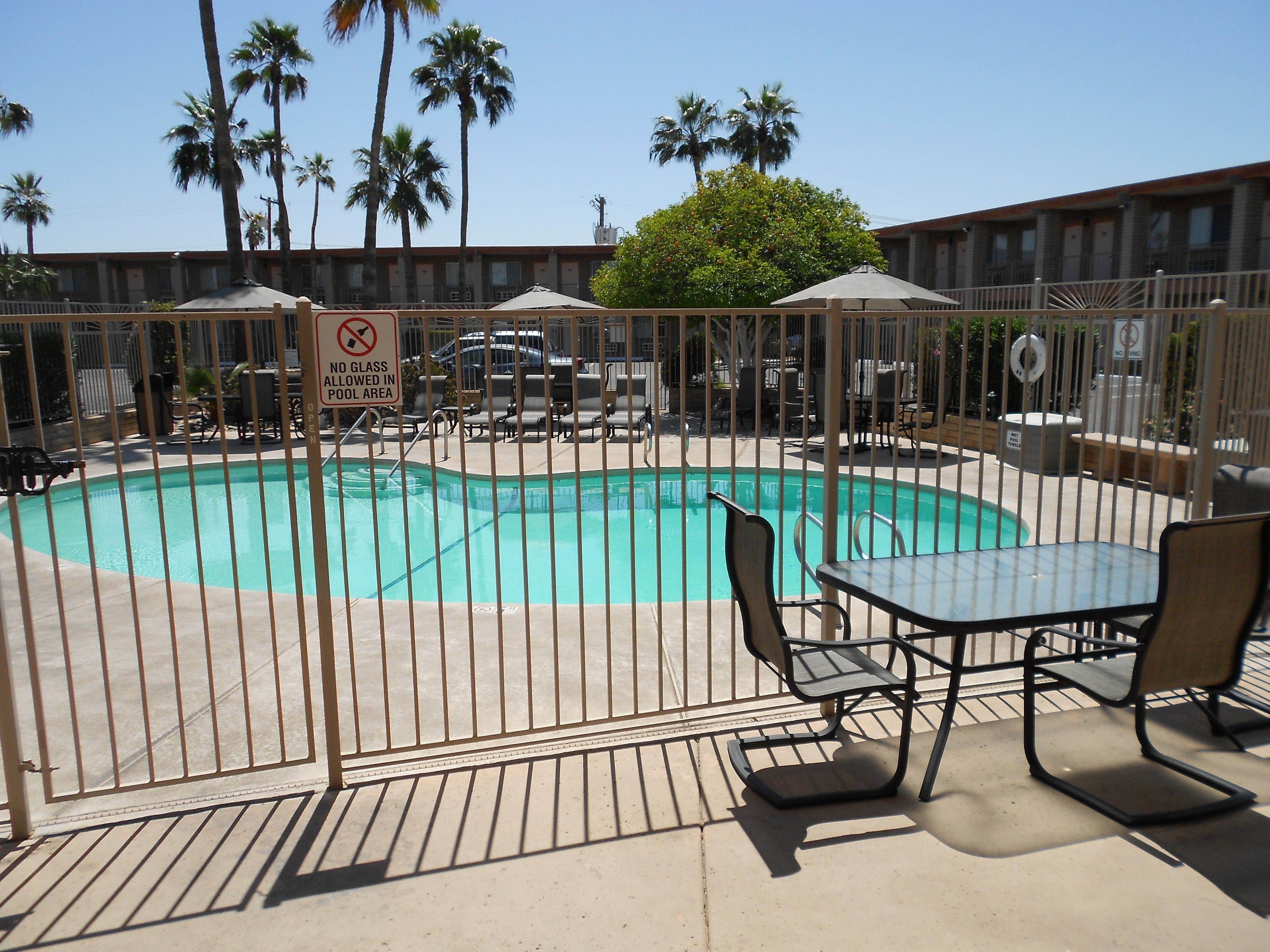 A swimming pool with a no glass allowed sign, surrounded by a fence, and shaded by umbrellas.