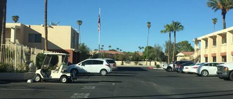 A parking lot with several cars, a golf cart, and palm trees.