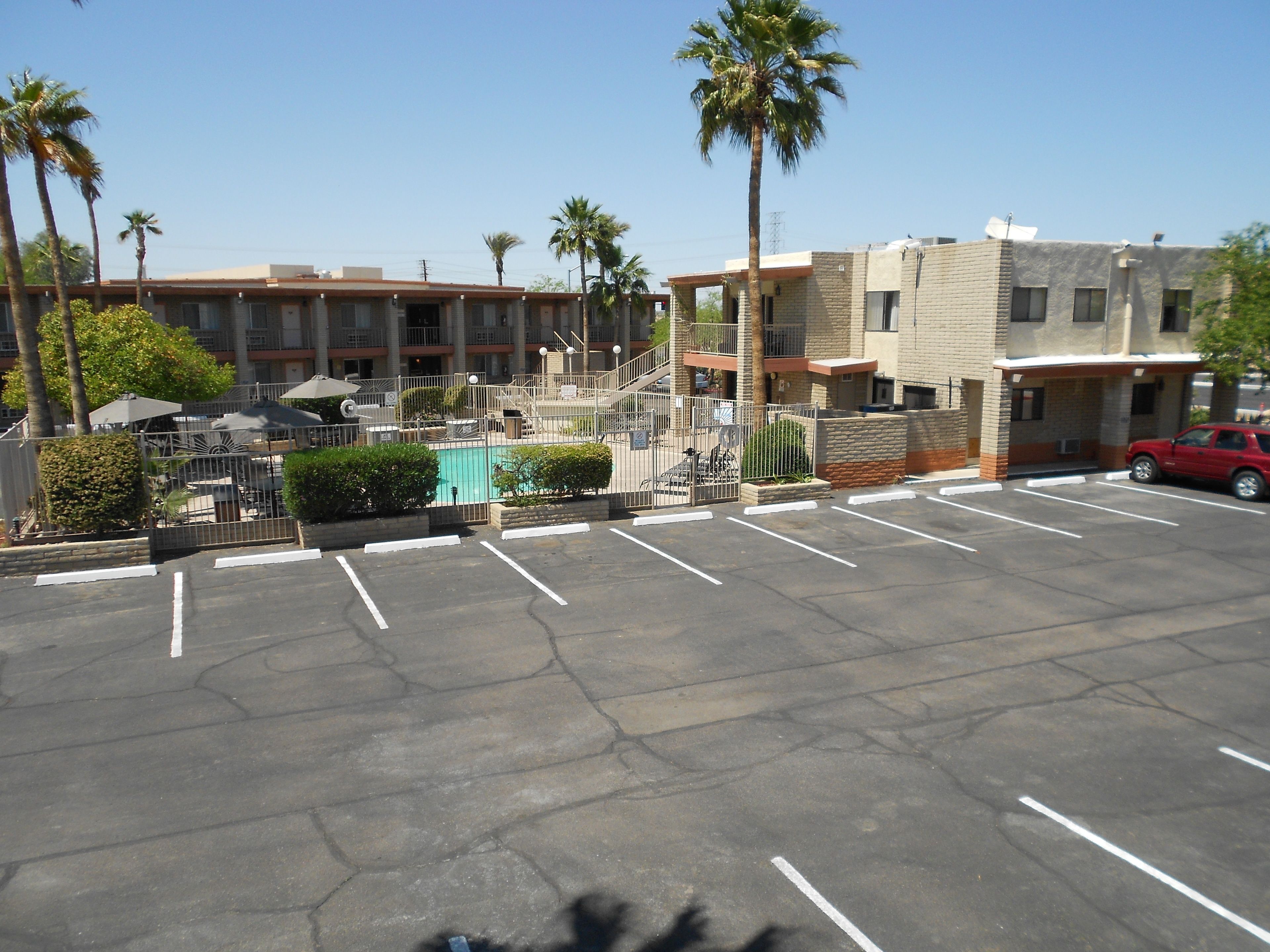 A parking lot with a swimming pool, palm trees, and a building with a brick facade.