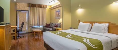 A hotel room with a large bed, a desk with a computer, a chair, and a couch.