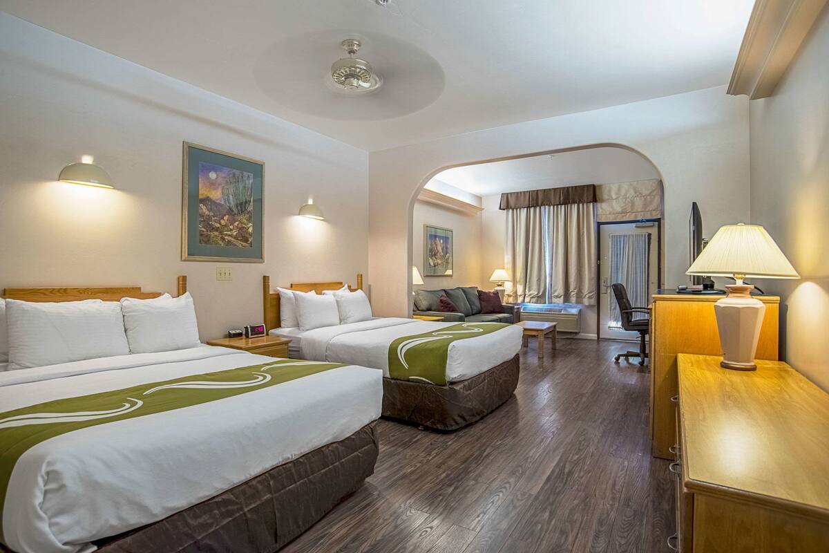 A hotel room with two beds, a desk, a chair, a lamp, and a painting on the wall.