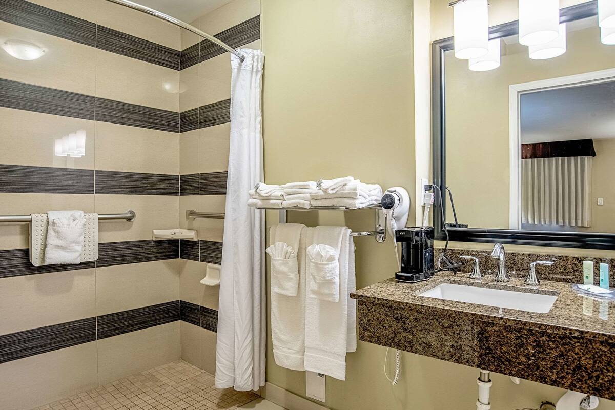 A bathroom with a shower, a sink, and a mirror. There are towels hanging on a rack and a hairdryer on the counter.