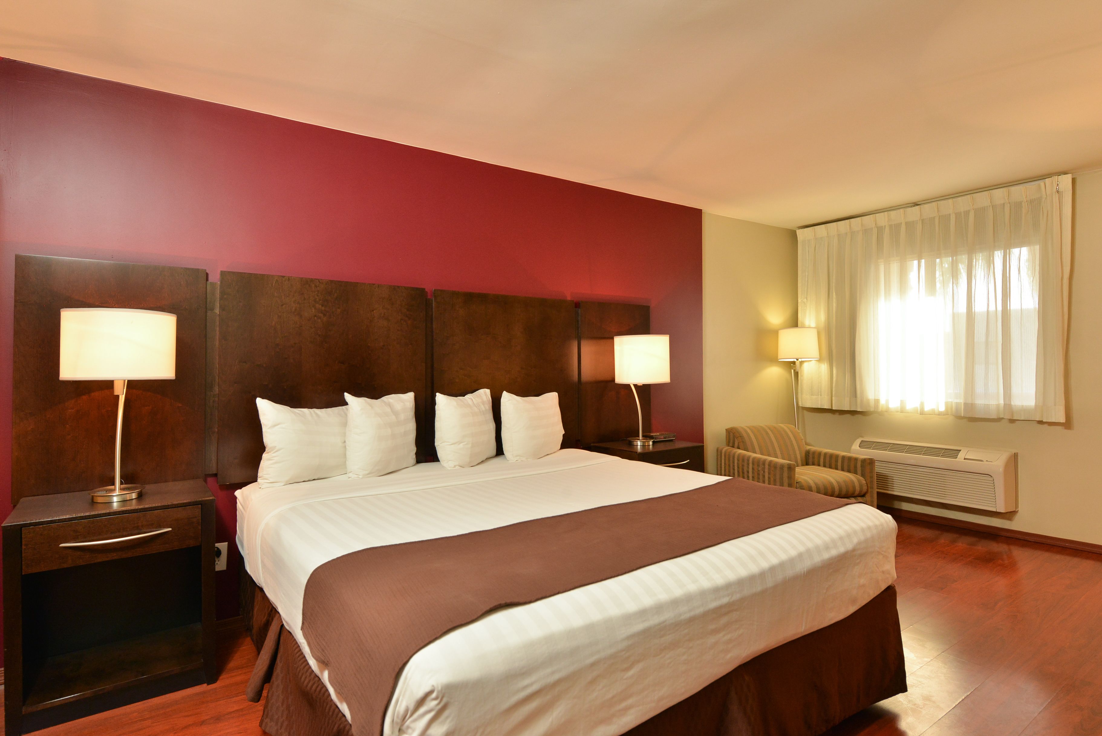 Habitación de hotel con una cama grande, dos mesitas de noche con lámparas, una silla y una ventana con cortinas.
