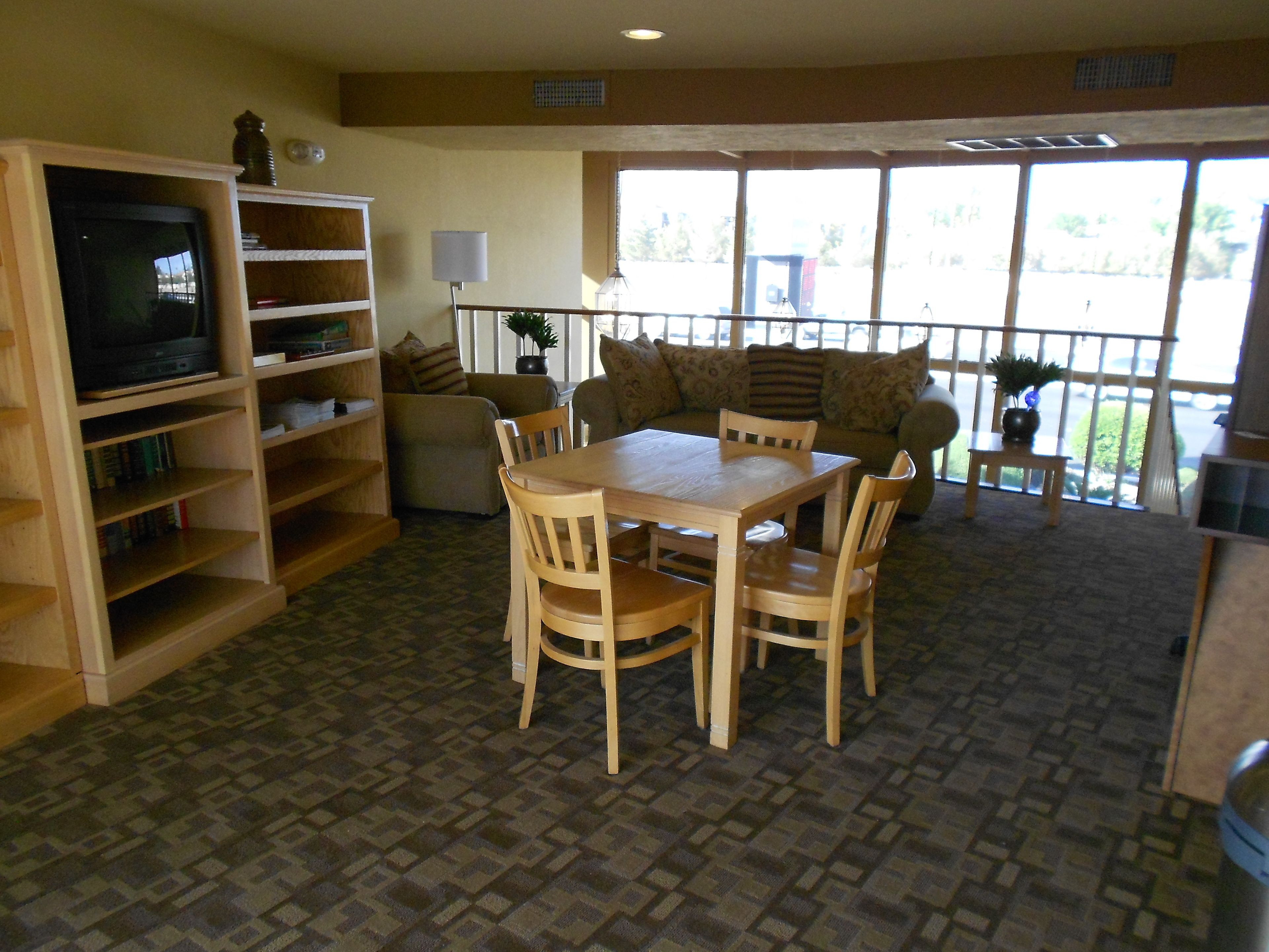 A dining area with a wooden table and chairs, a bookshelf, a television, and a large window with a view of the outdoors.