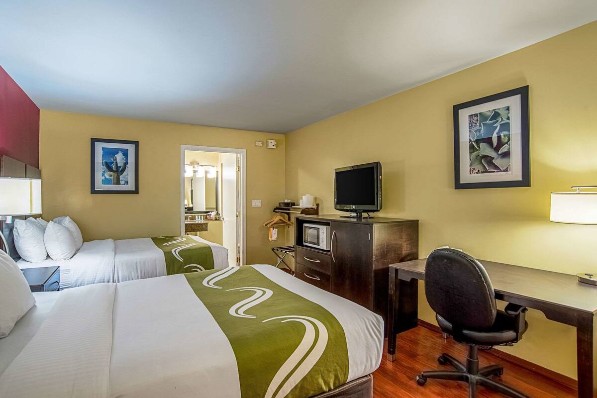 A hotel room with two beds, a desk, a chair, a television, and artwork on the walls.