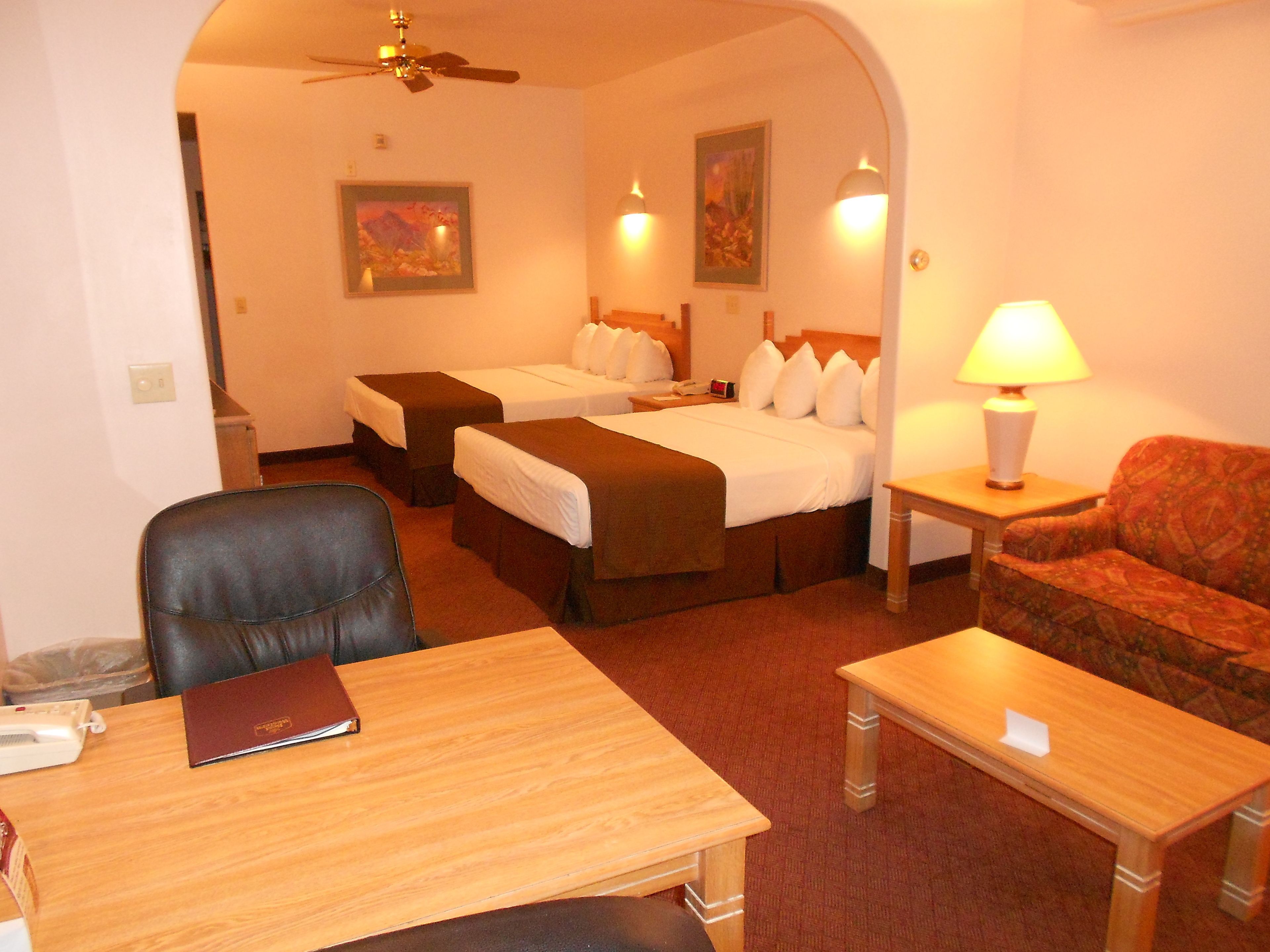 A hotel room with two beds, a desk, a chair, a sofa, and a lamp.