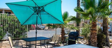 An outdoor patio with a table and chairs, a green umbrella, and a grill.