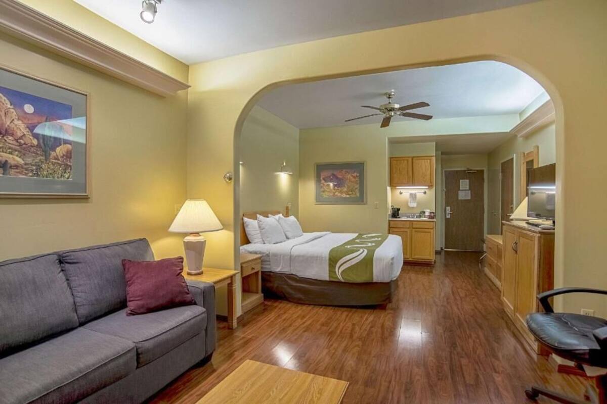 A compact hotel room with a bed, a sofa, a desk, and a kitchenette.