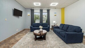 A living room with two sofas, a coffee table, a flat-screen TV, and a window with curtains.