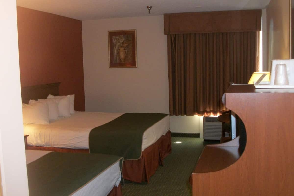 A hotel room with two beds, a desk, a chair, a painting on the wall, and a window with curtains.