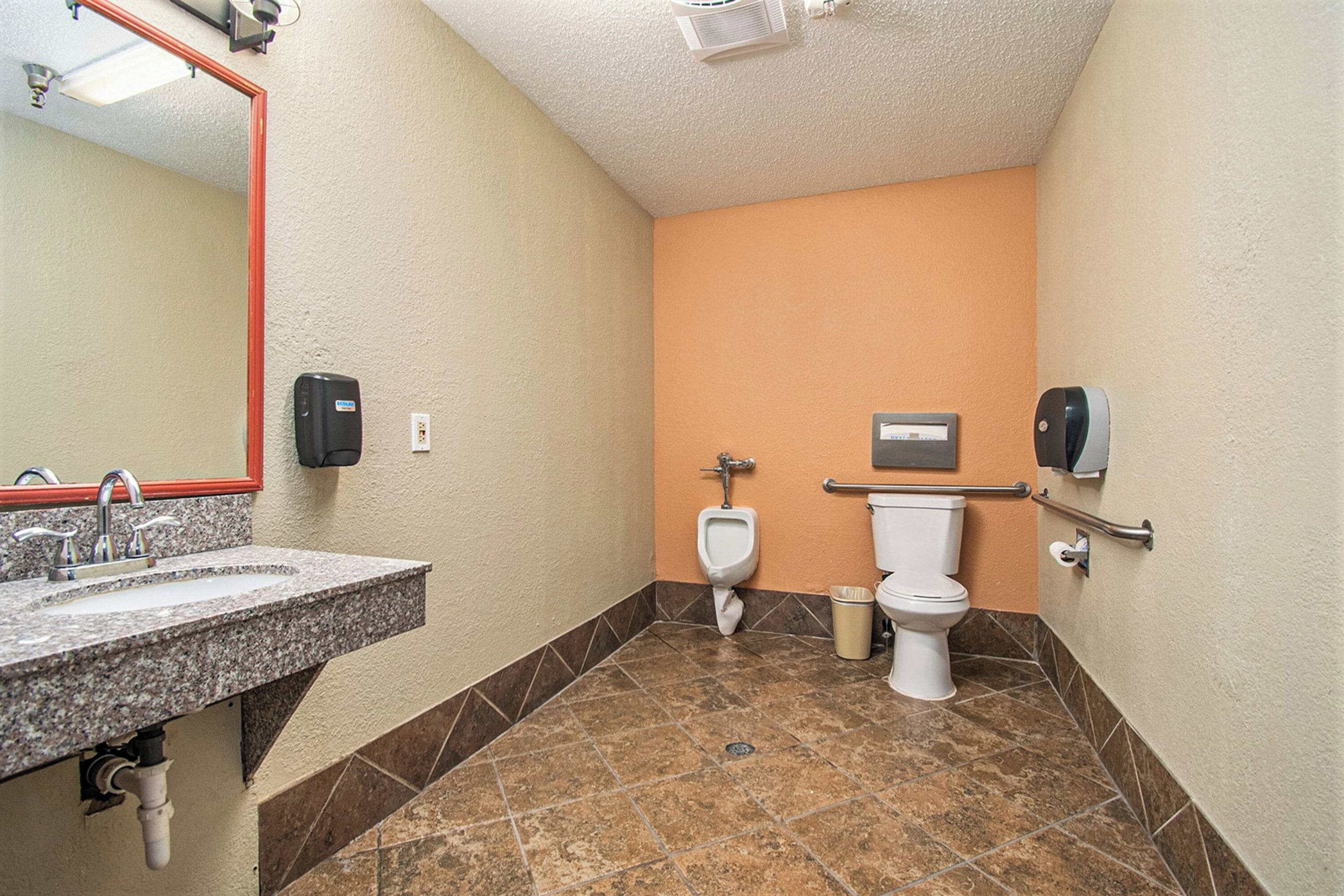 Un baño con lavamanos de granito, un orinal, un inodoro y un secador de manos.