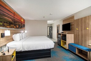 A hotel room with a bed, a TV, a desk, a bench, and a painting on the wall. - Days Inn & Suites by Wyndham Mt Pleasant (Mount Pleasant)