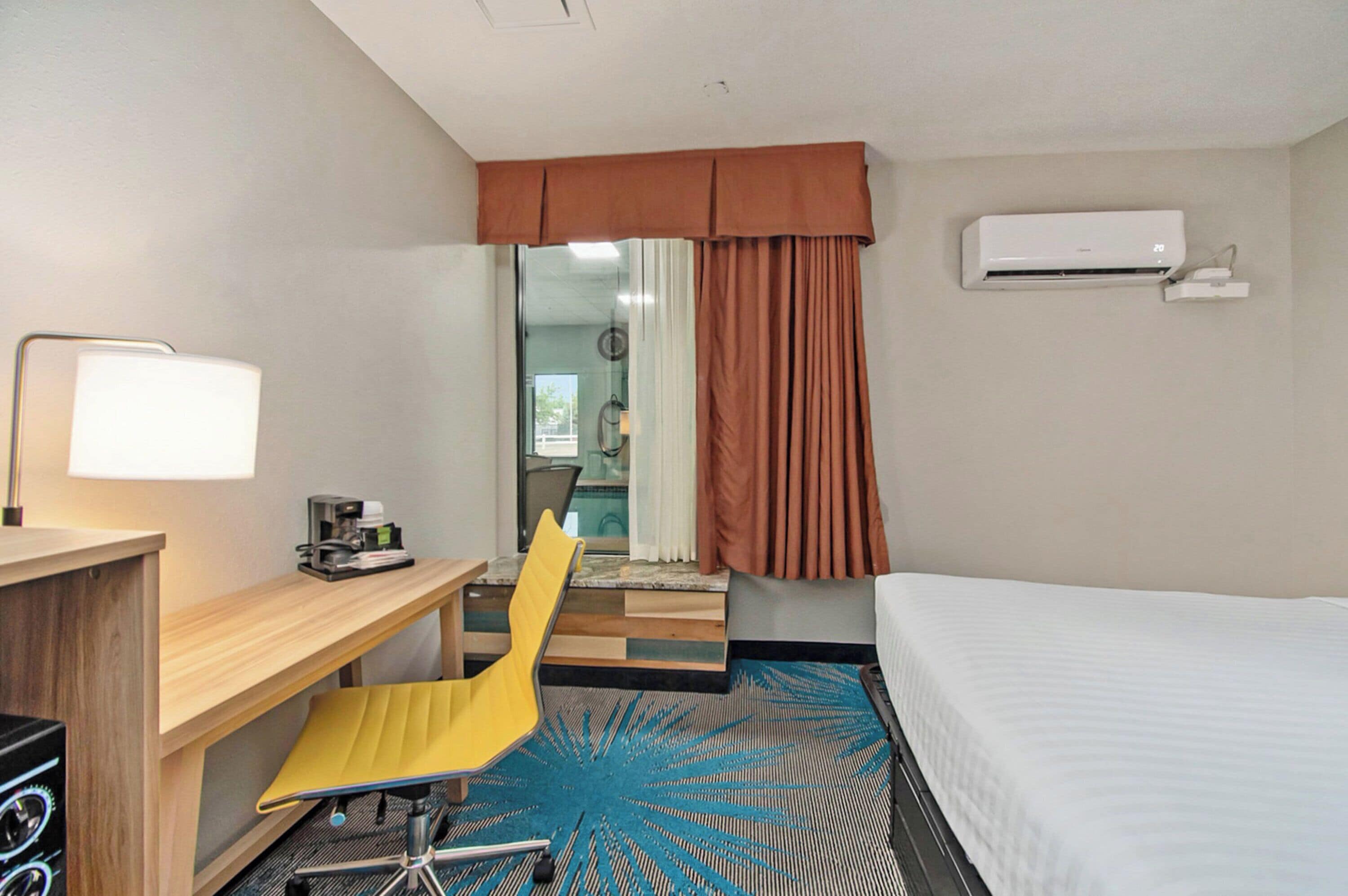 Una habitación de hotel con una cama, un escritorio con silla, una cafetera y un equipo de aire acondicionado.