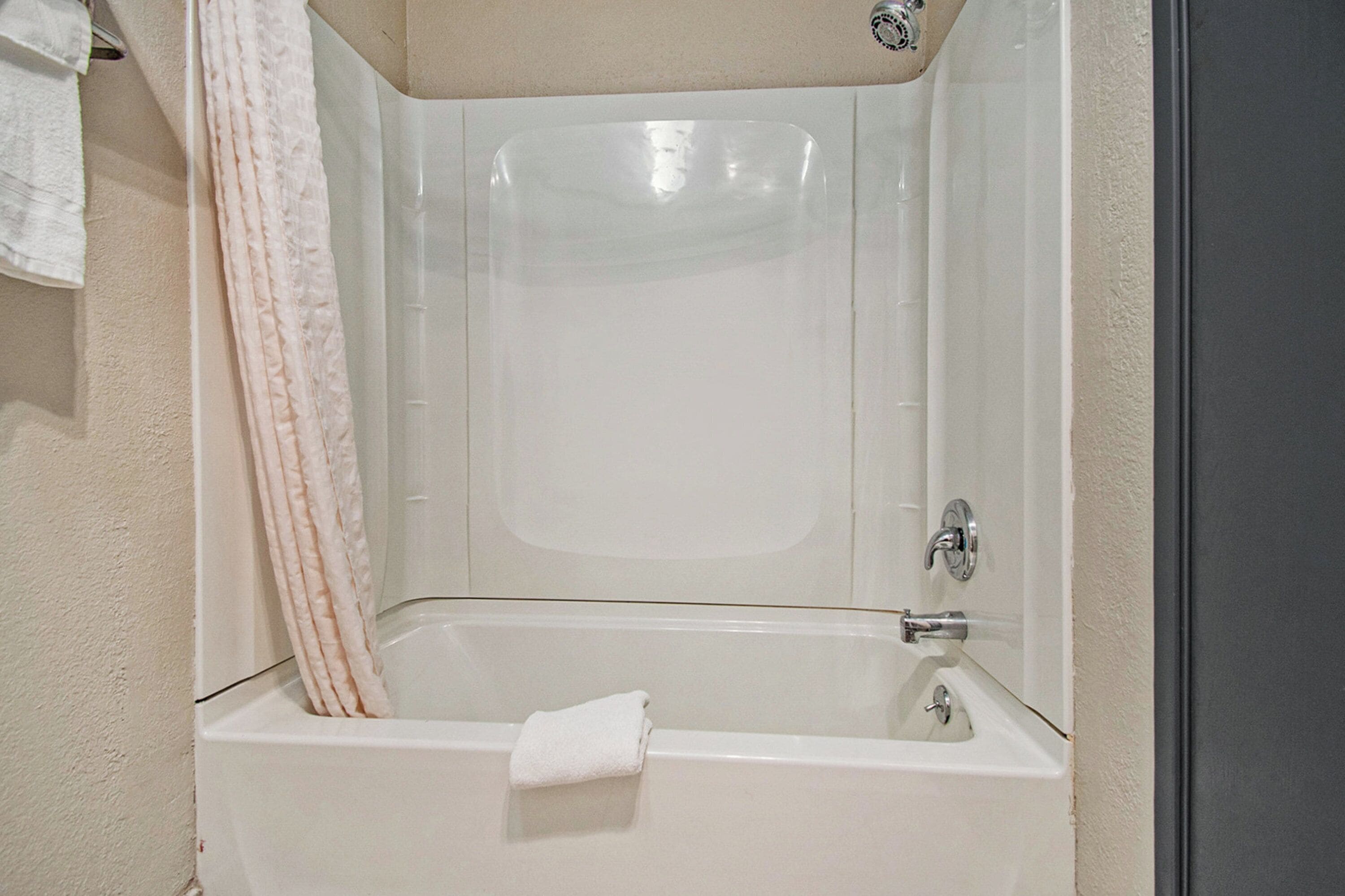 A white bathtub with a shower curtain, a towel, and a faucet.