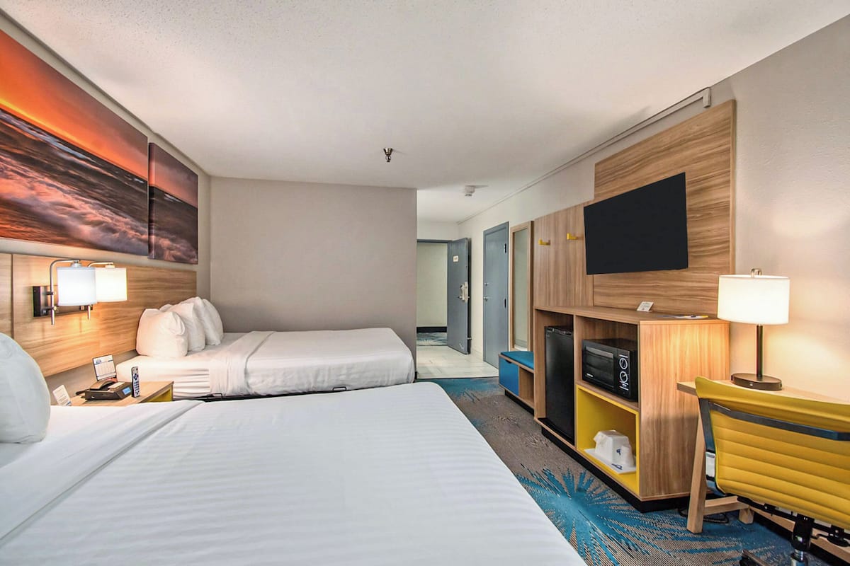 A hotel room with two beds, a TV, a desk with a chair, and a microwave.
