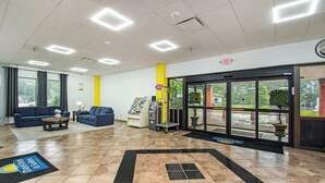 A lobby with a blue sofa, a coffee table, a reception desk, an ATM, and a glass door entrance.