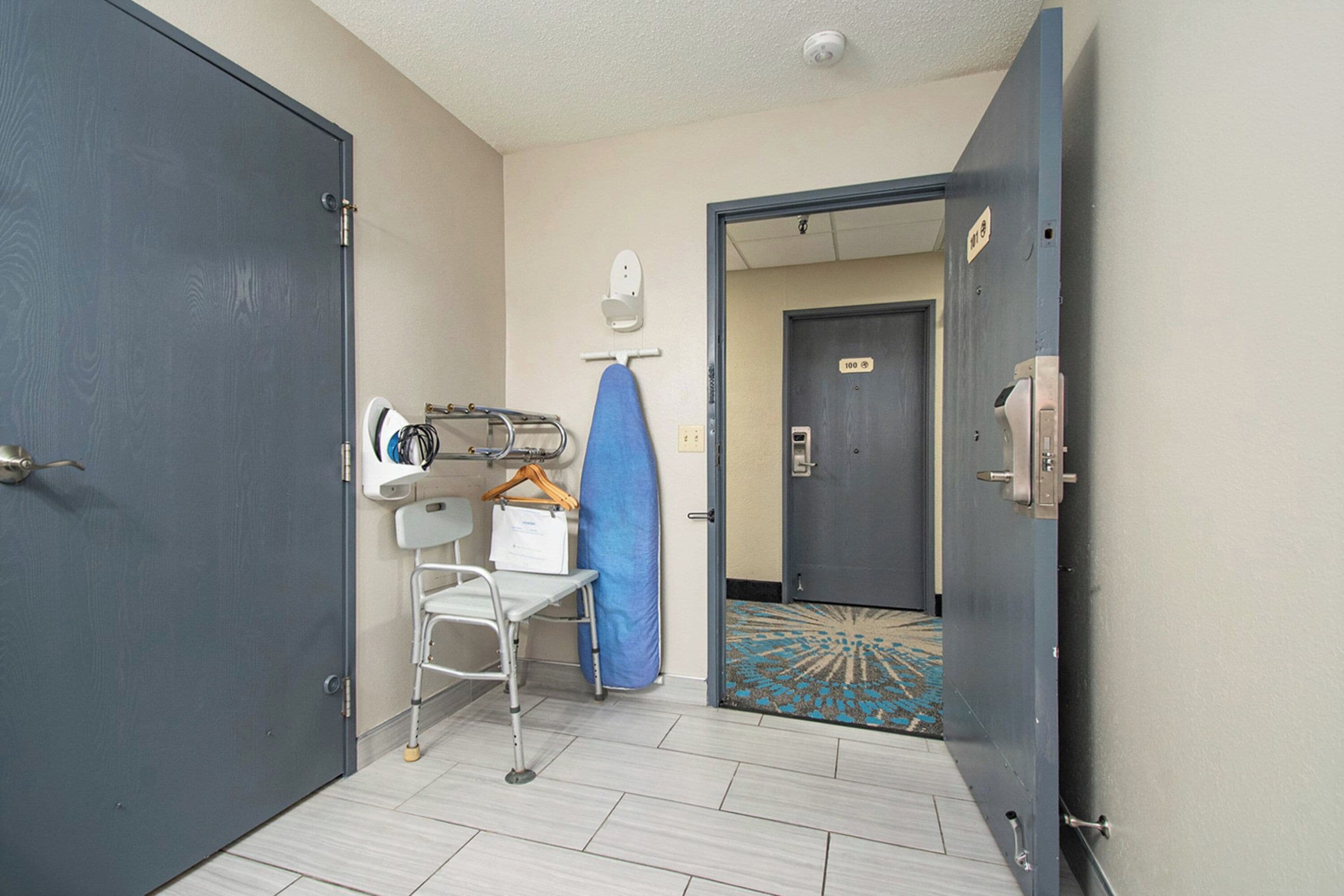 Ein Hotelzimmer mit Bett, Nachttisch, Stuhl, blauer Duschvorhang und einer Tür zu einem anderen Raum.