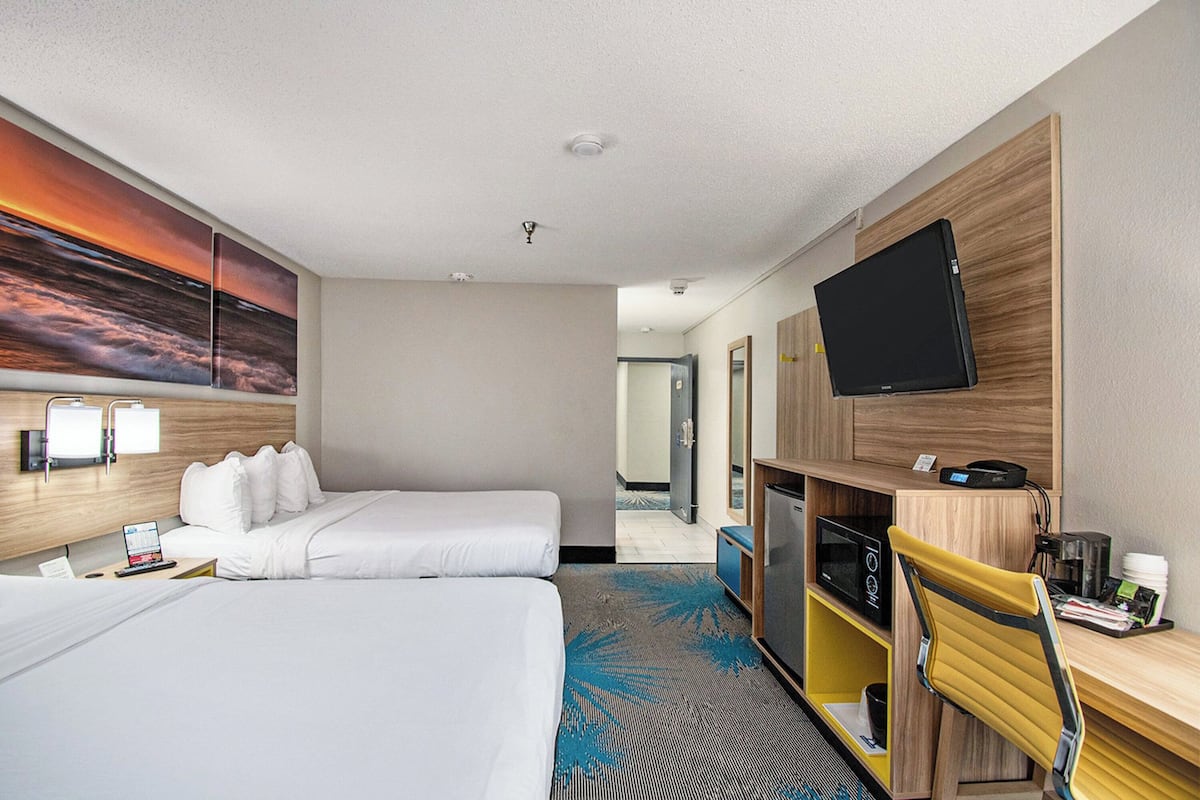 A hotel room with two beds, a flat-screen TV, a desk with a chair, a microwave, and a coffee maker.