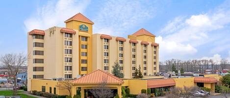 A multi-story hotel with a central courtyard, parking lot, and a prominent entrance with a covered area.