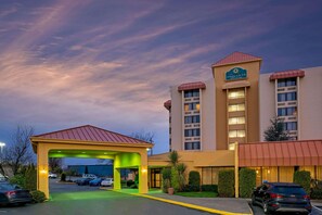 A hotel with a covered entrance, a parking lot, and a building with a sign reading "La Quinta Inn & Suites".