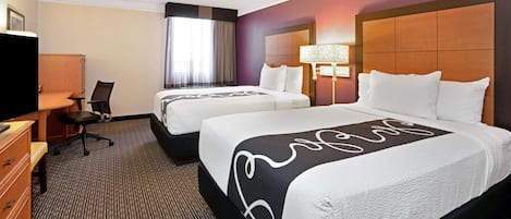 A hotel room with two beds, a desk, a chair, a TV, and a window with curtains.
