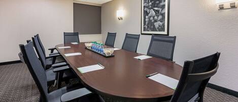 Une salle de conférence avec une longue table, des chaises noires et un tableau encadré au mur.