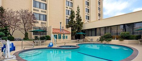 A hotel with a swimming pool, lounge chairs, and a covered area with umbrellas.