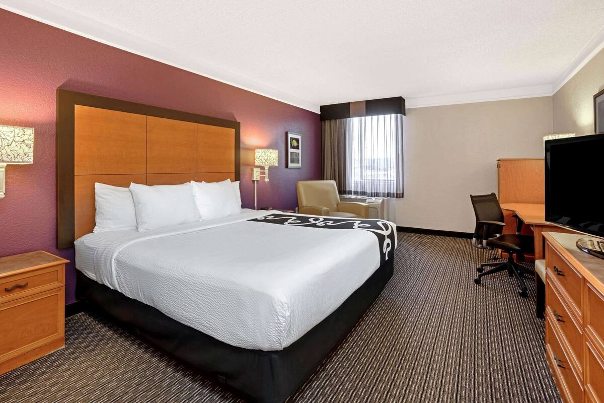 Quarto de hotel com uma cama grande, uma escrivaninha com cadeira, televisão e cómoda.